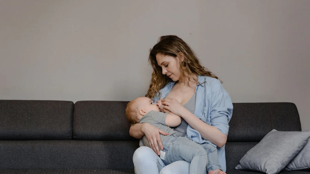 Mère allaitant son bébé sur un canapé, illustrant la prise du sein et le confort d’allaitement