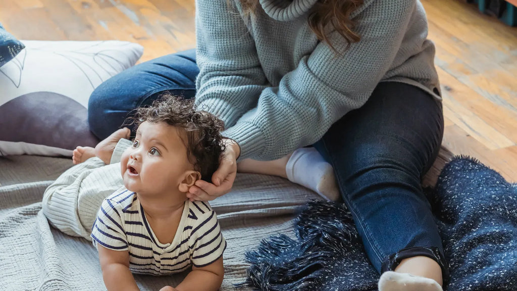 Parent allongé près de son bébé éveillé sur un tapis au sol pendant un temps sur le ventre surveillé